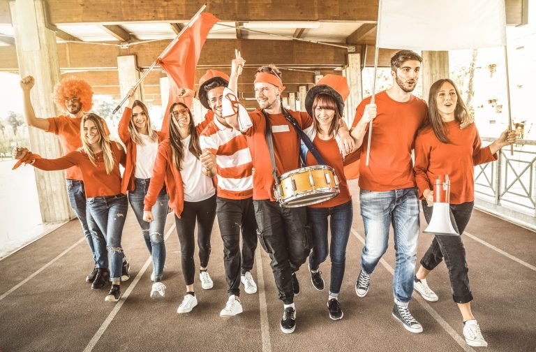 Football supporter fans friends cheering and walking to soccer cup match at intenational stadium - Young people group with red and white t-shirts having excited fun on sport world championship concept