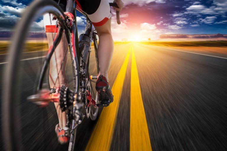 Male cyclist on bike path, view from the rear wheel. Cycling on asphalt road. Sportsman rides on bicycle, bycyclist on workout